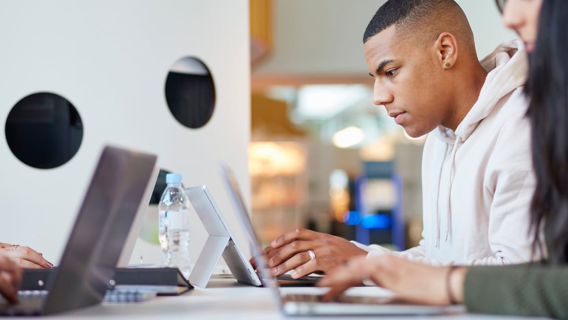 Two colleagues working on laptops side by side at a shared office desk