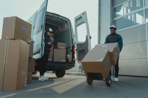 Workers unloading delivery boxes from a van, illustrating rising postal costs impacting IT budgets