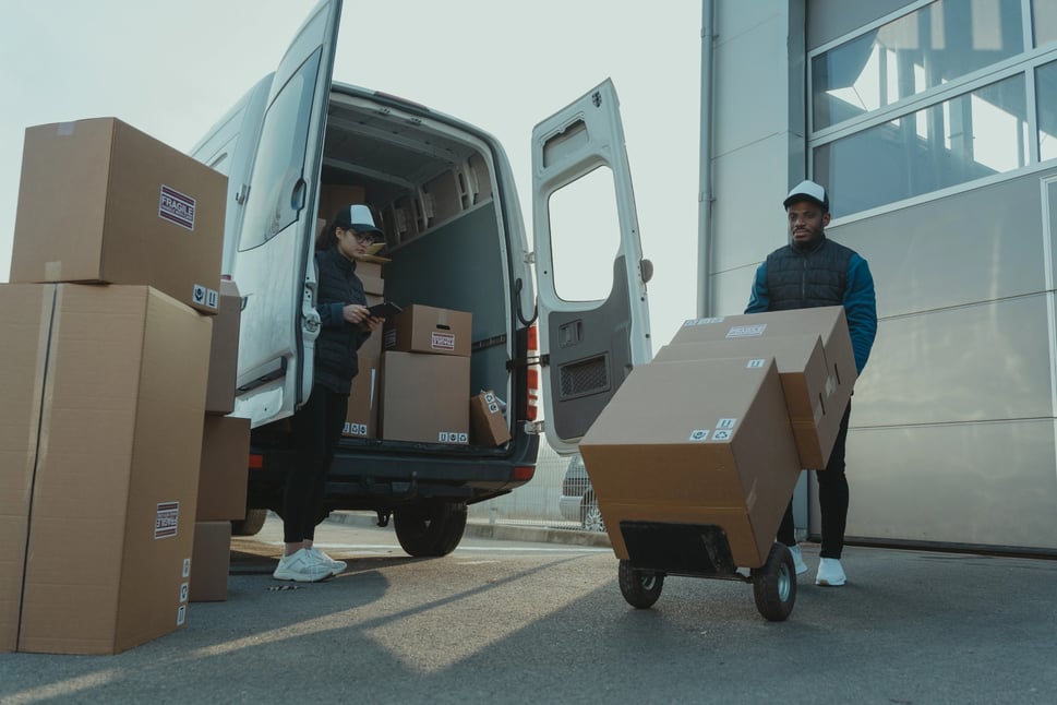 Workers unloading delivery boxes from a van, illustrating rising postal costs impacting IT budgets
